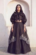 Black crop raw silk lehenga with bow-tie puff-sleeve top, full-length front view against an arch
