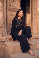 Black cutdana short shirt with silver and pink floral work and black trousers, seated