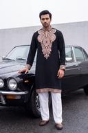Black embroidered kurta with white shalwar worn beside a vintage car in a black and white street scene