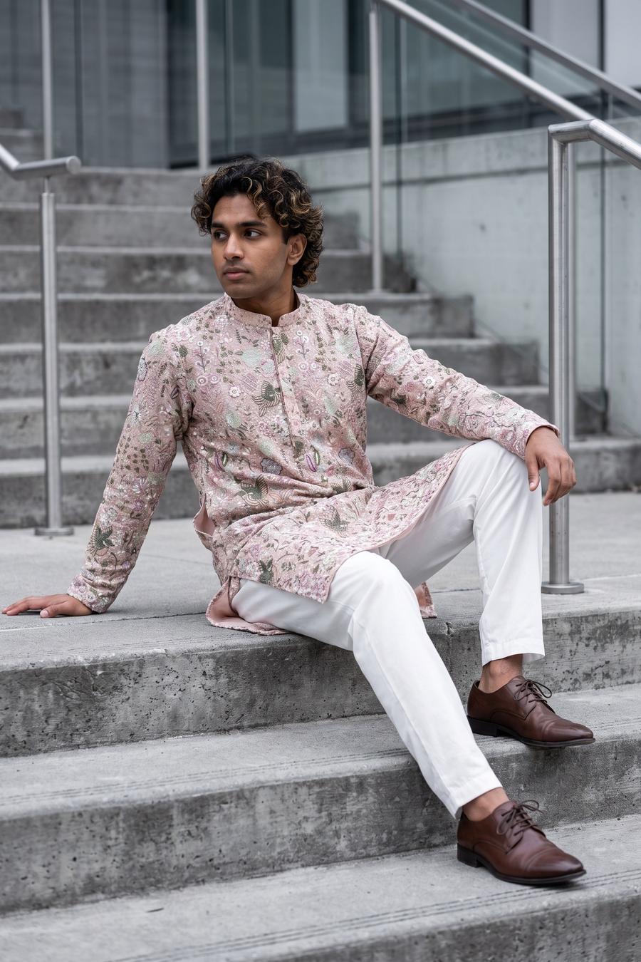Blush pink embroidered kurta with white shalwar, model seated in a cool toned city setting
