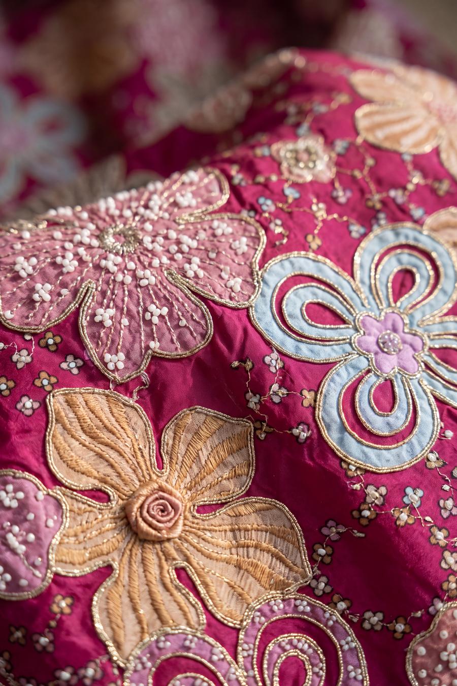 Close up of fuchsia silk with rose, camel, sky blue and olive florals outlined in gold, seed beads