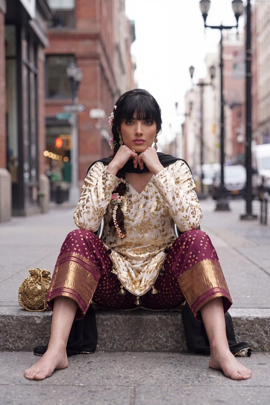 Ivory gold muqesh shirt seated, wine trousers with wide gold borders at the hem in view