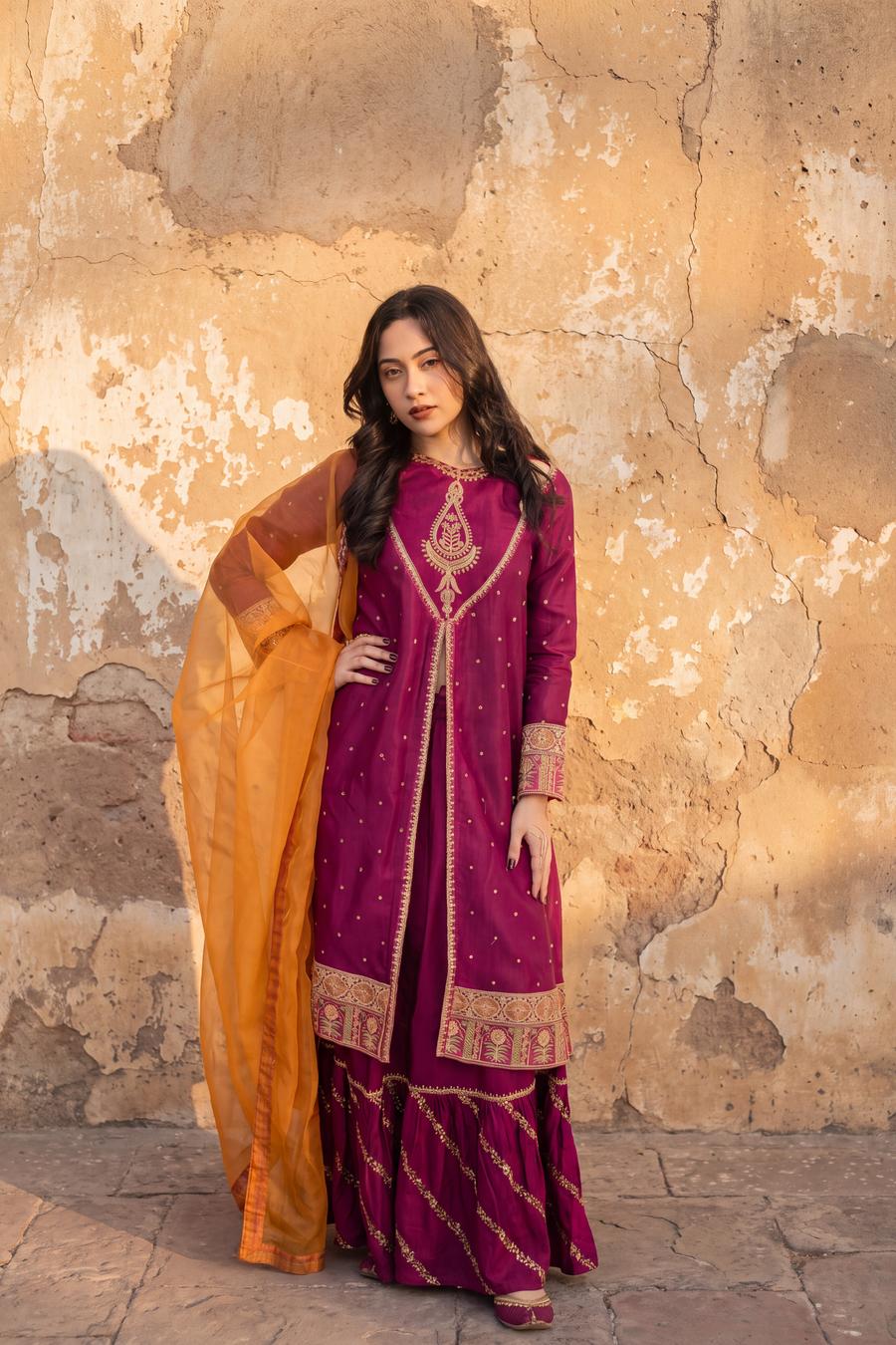 Magenta long shirt and sharara, standing with one hand on the hip and the marigold organza dupatta held open