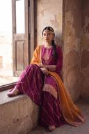 Magenta long shirt and sharara with marigold dupatta, seated by a window, styled with a side braid and pearl headpiece