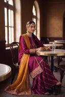 Magenta long shirt and sharara with marigold dupatta, seated at a table showing the gold border on the sharara