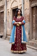 Maroon raw silk anarkali with gold floral embroidery and a sky blue net dupatta, full length front view