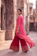 Red tie dye long shirt with crushed red izzar pants and a flowing pink dupatta, three quarter back view