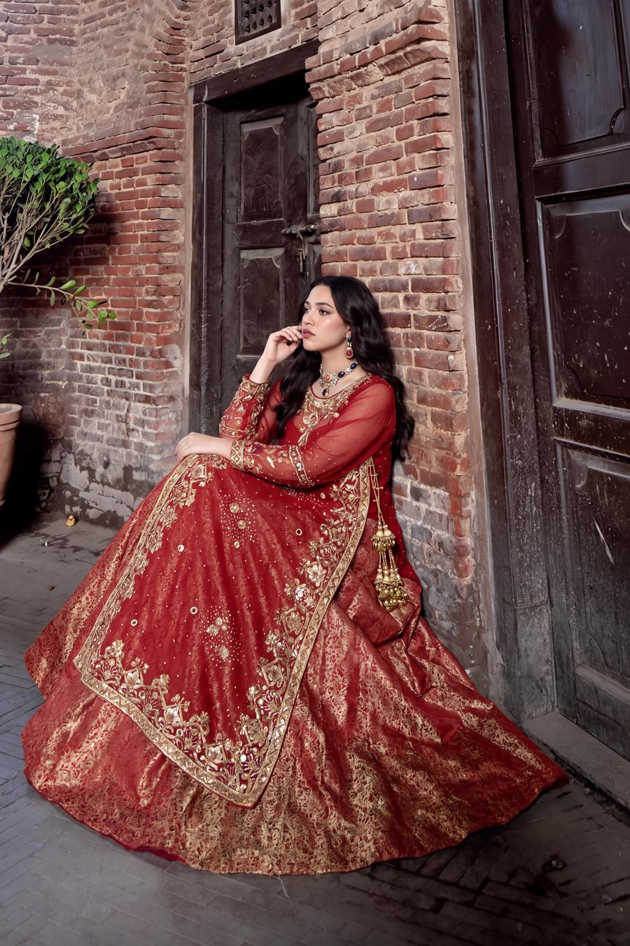 Red long shirt lehenga seated, flared gold brocade skirt and muqesh border spread across the floor