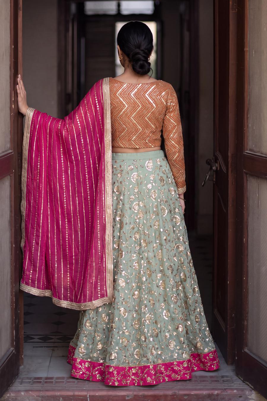 Back view of sage floral lehenga and tangerine chevron sequin top, magenta dupatta over one arm