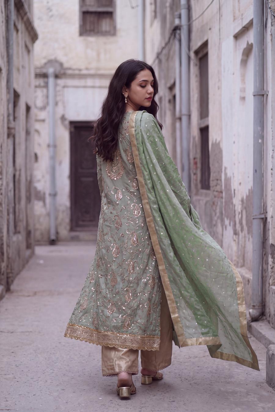 Back view of sage green embroidered shirt and gold trousers, dupatta trailing in motion